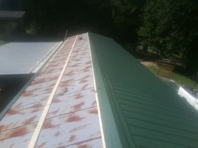 Old rusted panels beside newly installed green metal roofing — Wind Damage Roof Repair by Roofing Brothers in Sturgis